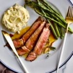 steak slices on a plate with mashed potatoes and asparagus.