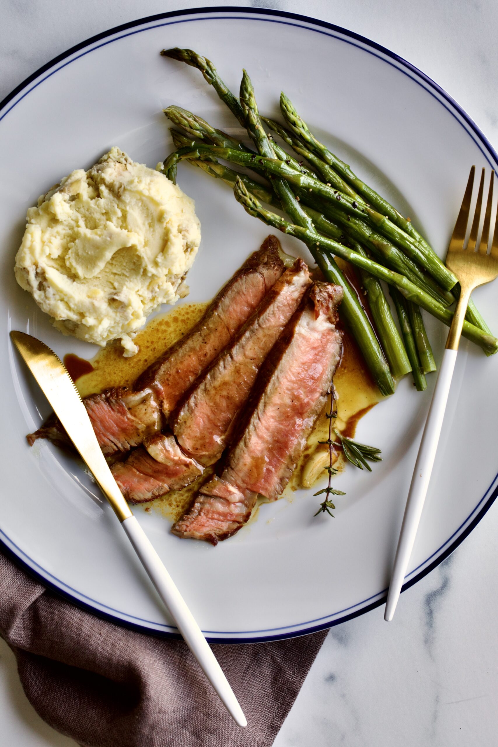 steak slices on a plate with mashed potatoes and asparagus.