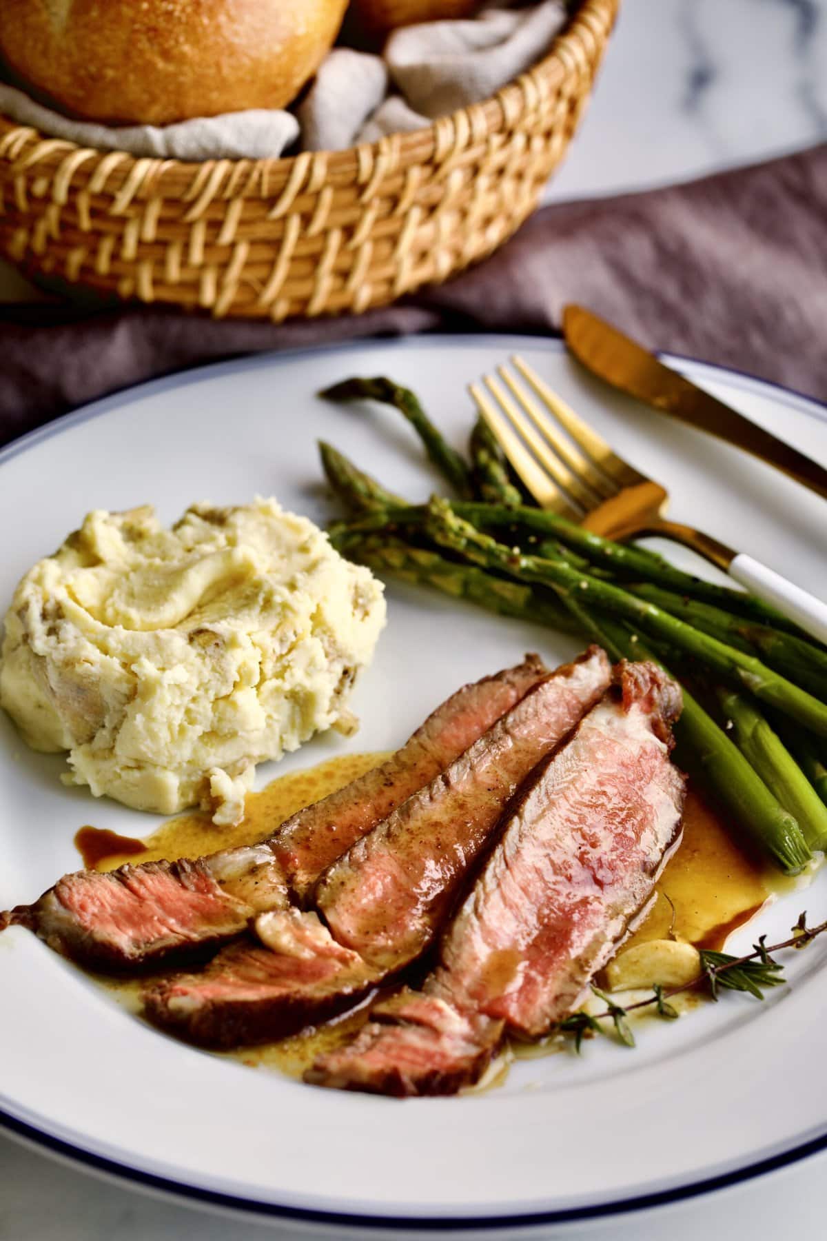 steak slices on a plate with mashed potatoes and asparagus. with fork and knife on the plate.