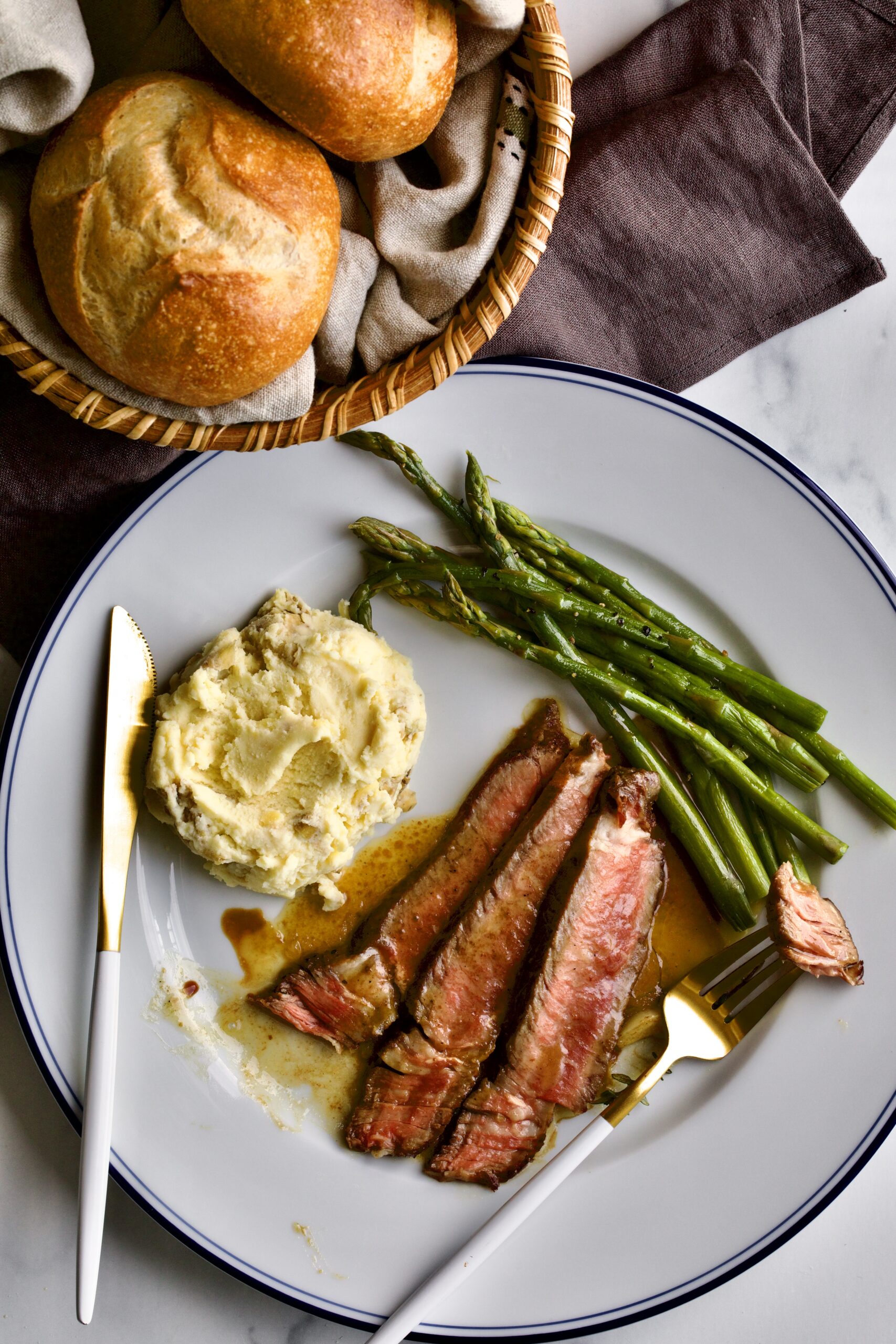 steak slices on a plate with mashed potatoes and asparagus. with fork with a bread roll.