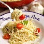plate of angel hair pasta with herbs and garlic. fork full of pasta twirled on a fork.