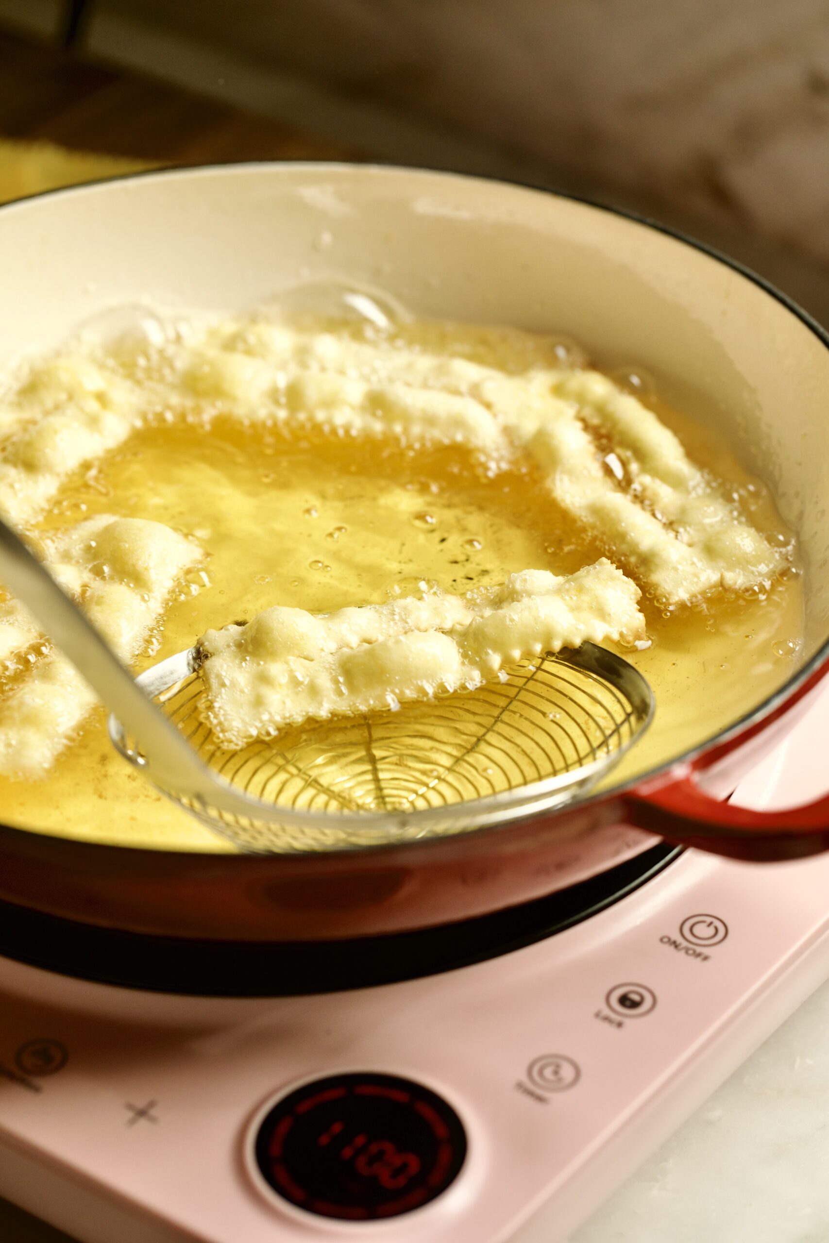 process of making chiacchiere: frying the dough frying in the hot oil taking out with slotted spoon.