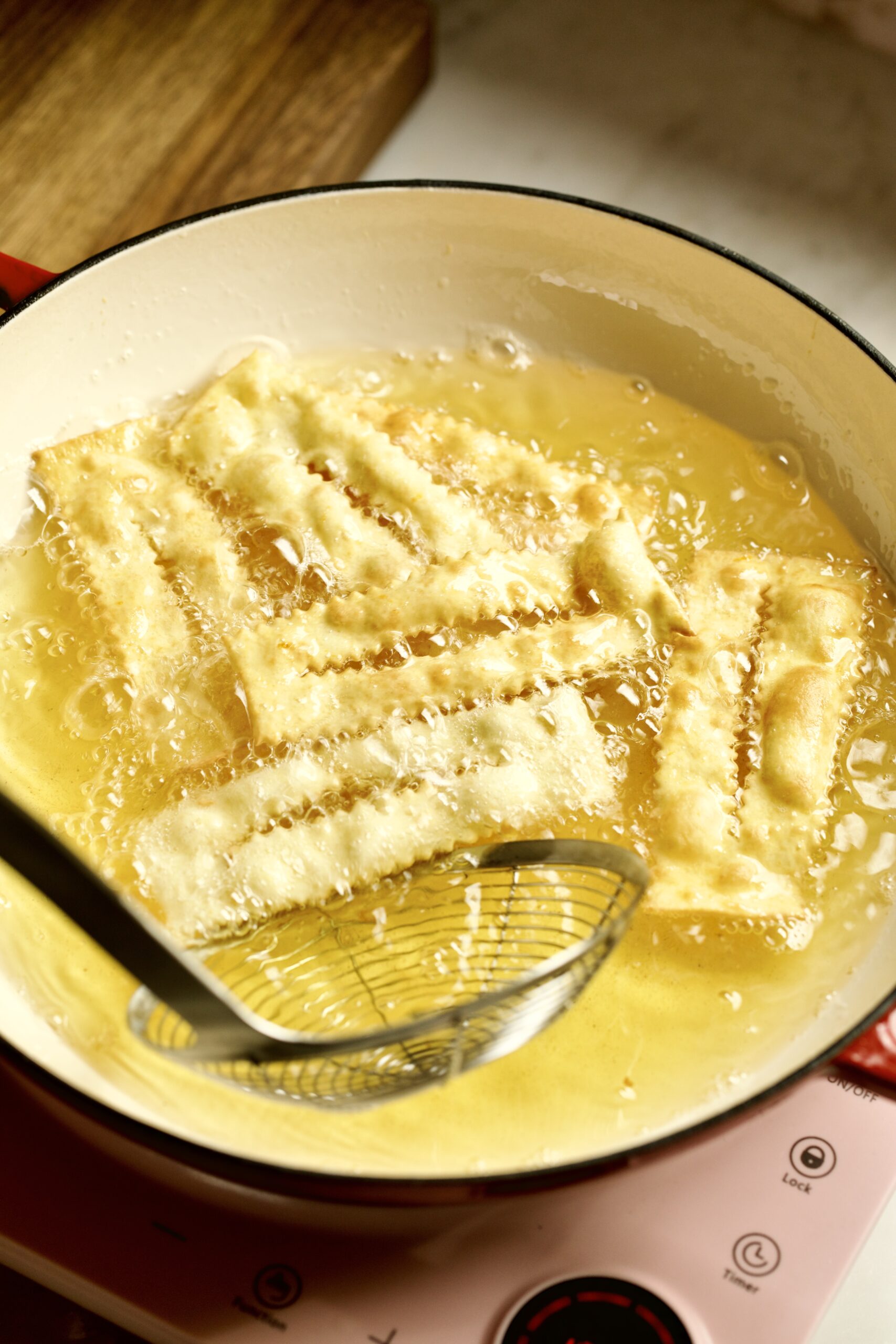 process of making chiacchiere: frying the dough frying in the hot oil taking out with slotted spoon.