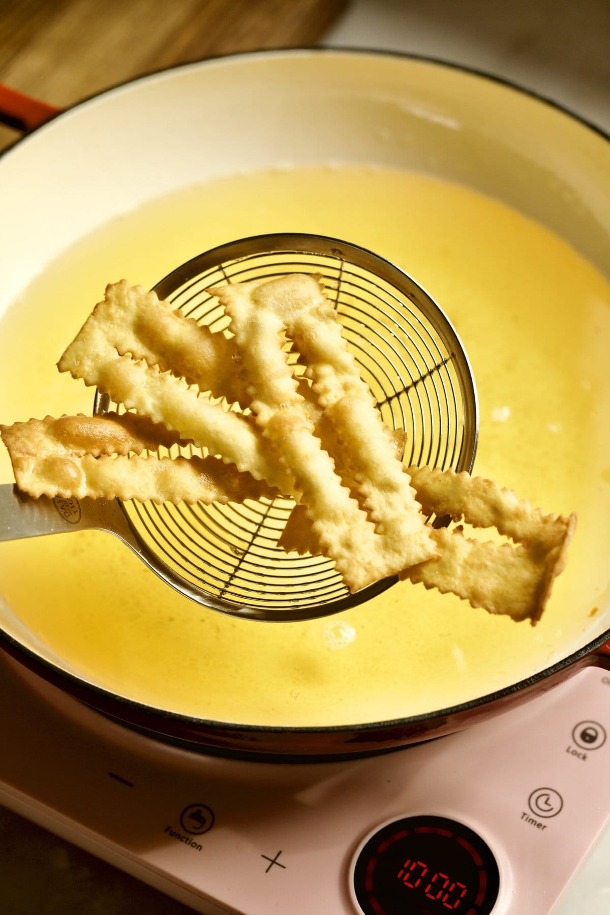 process of making chiacchiere: frying the dough frying in the hot oil taking out with slotted spoon.