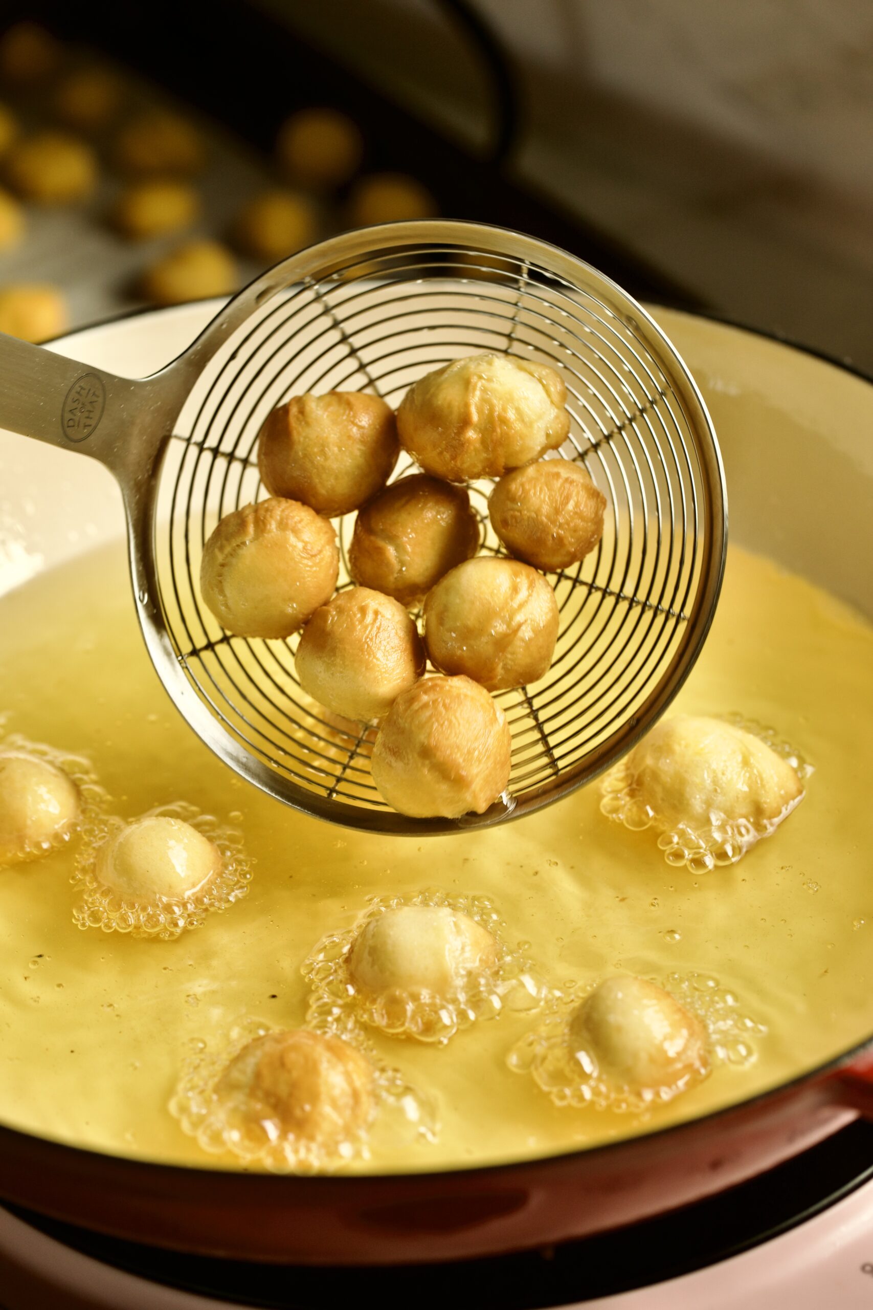 process of making authentic struffoli recipe: dough balls taken out of frying oil with slotted spoon.