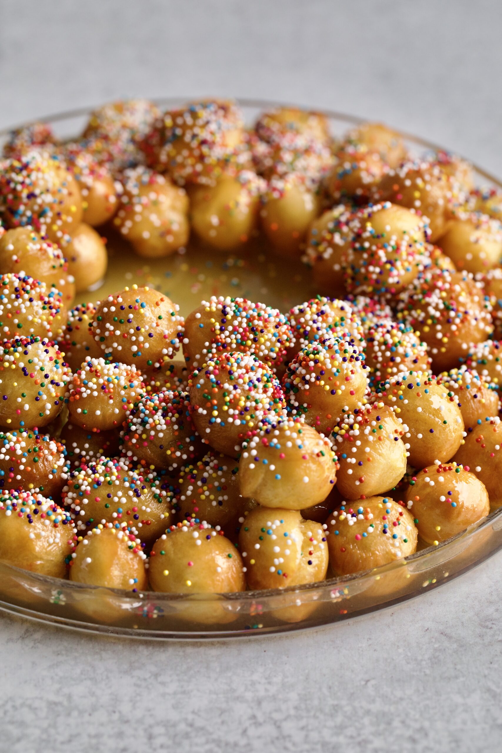 close up honey dough balls with sprinkles on a serving platter- wreath shape.