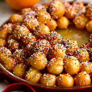 Struffoli honey dough balls with sprinkles on a serving platter in a wreath shape.