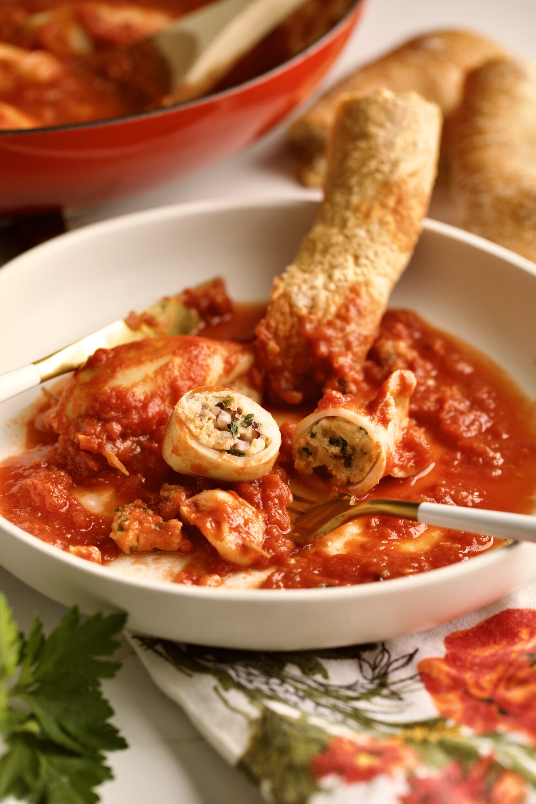 stuffed calamari with tomato sauce served in a plate with crusty bread . Cut open and bite taken out of calamari.