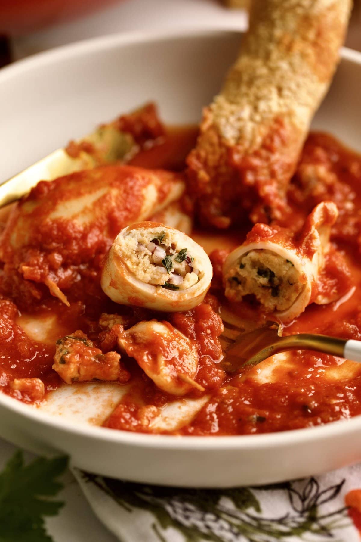 stuffed calamari with tomato sauce served in a plate with crusty bread . Cut open and bite taken out of calamari.