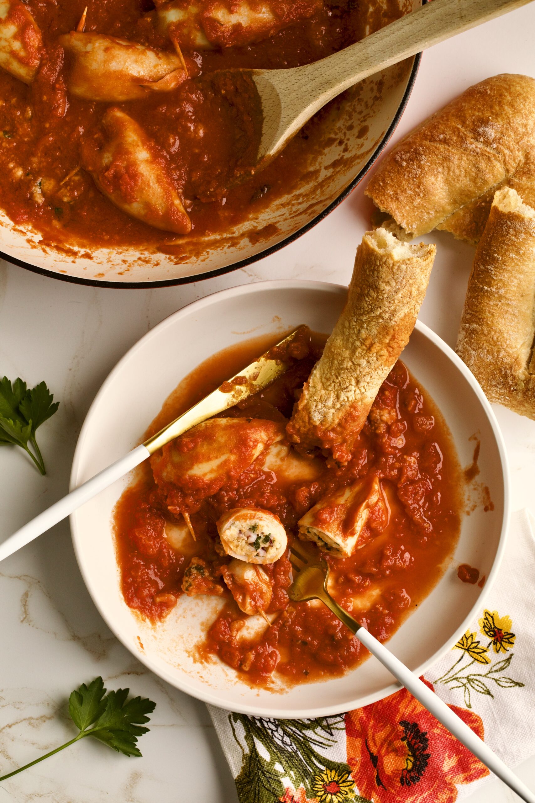 stuffed calamari with tomato sauce served in a plate with crusty bread . Cut open and bite taken out of calamari.