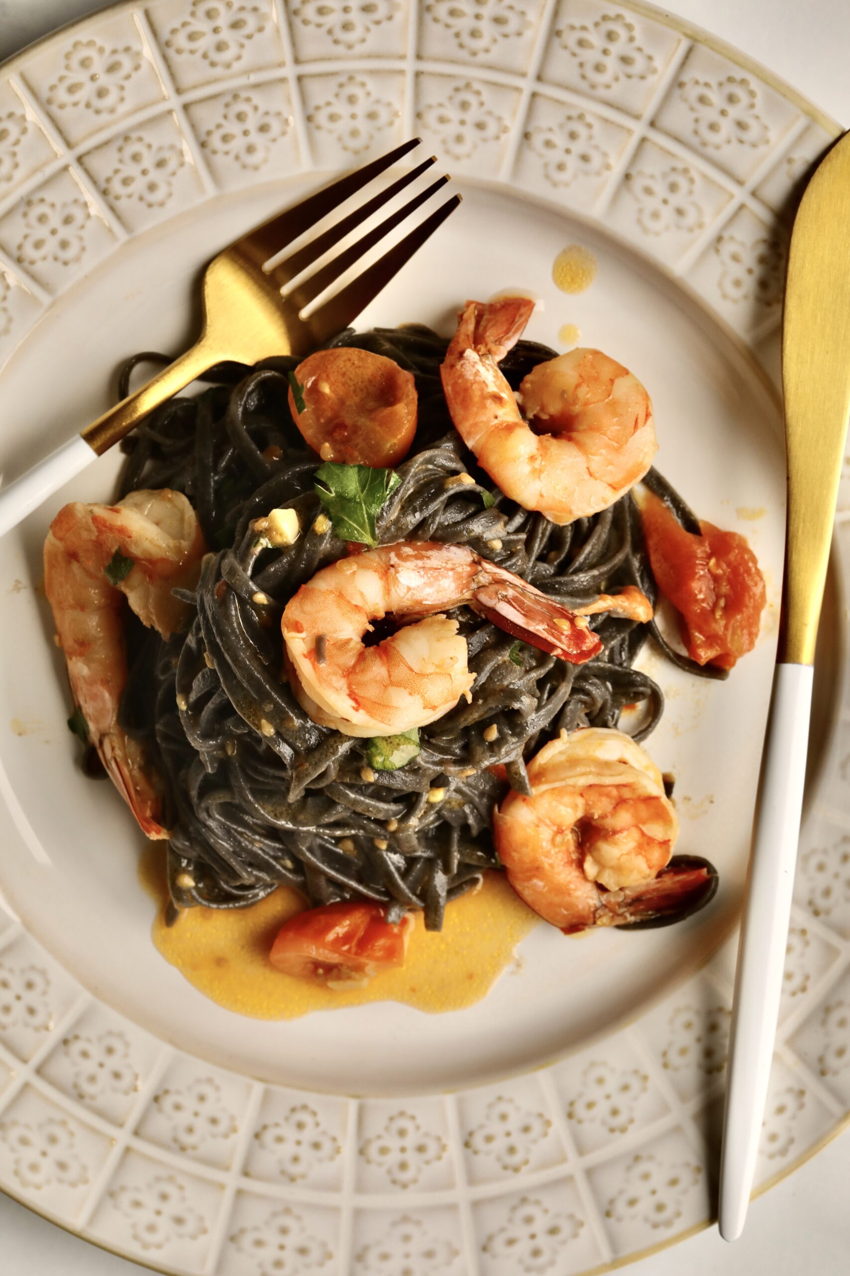 squid ink pasta with shrimp on a plate ready to eat. Fork and knife on plate.