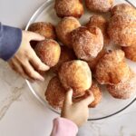Zeppole Recipe (Easy Italian Donuts)children's hands reaching for zeopple recipe that are on a plate.