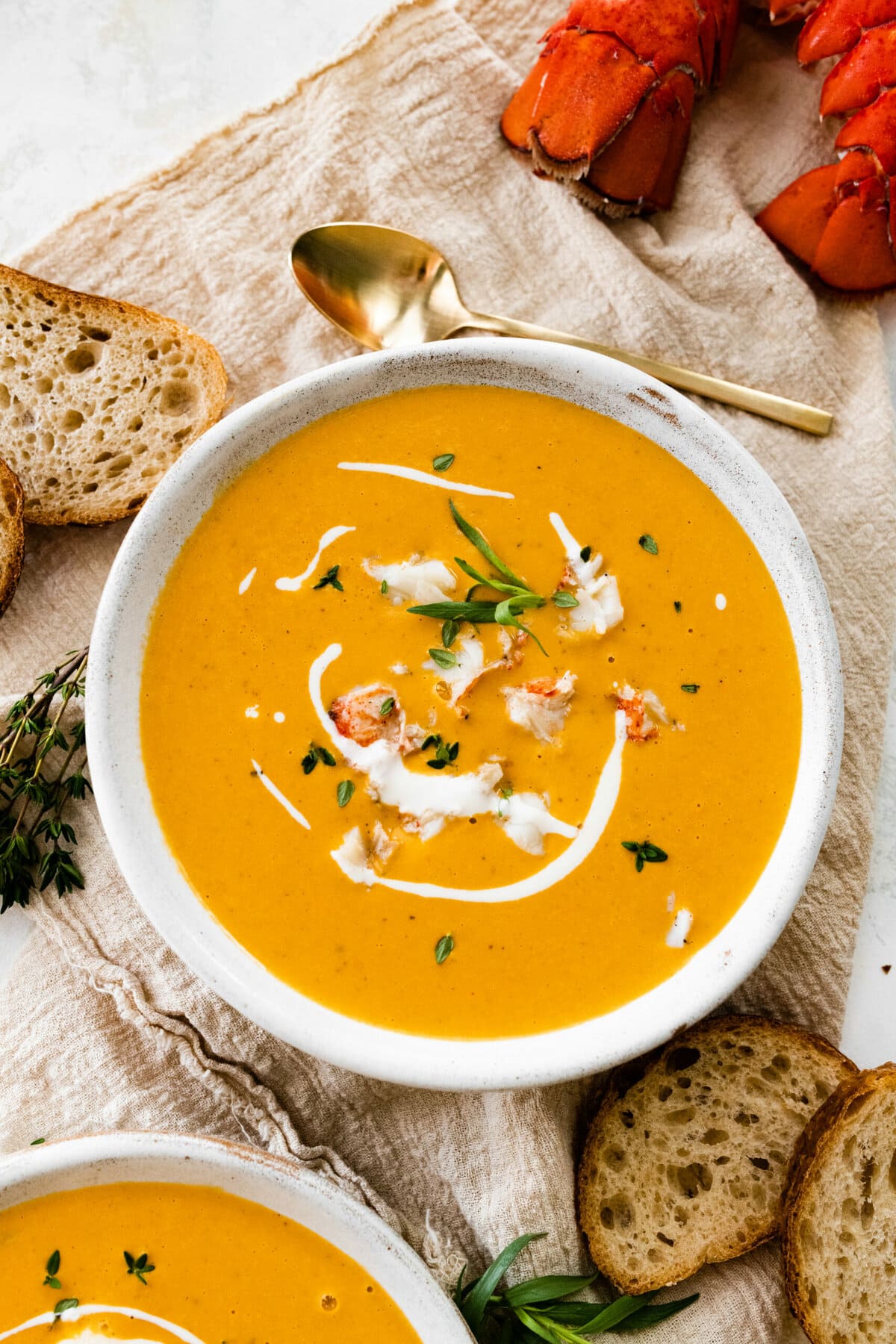 lobster bisque in a bowl with drizzle of cream and bread on the side.