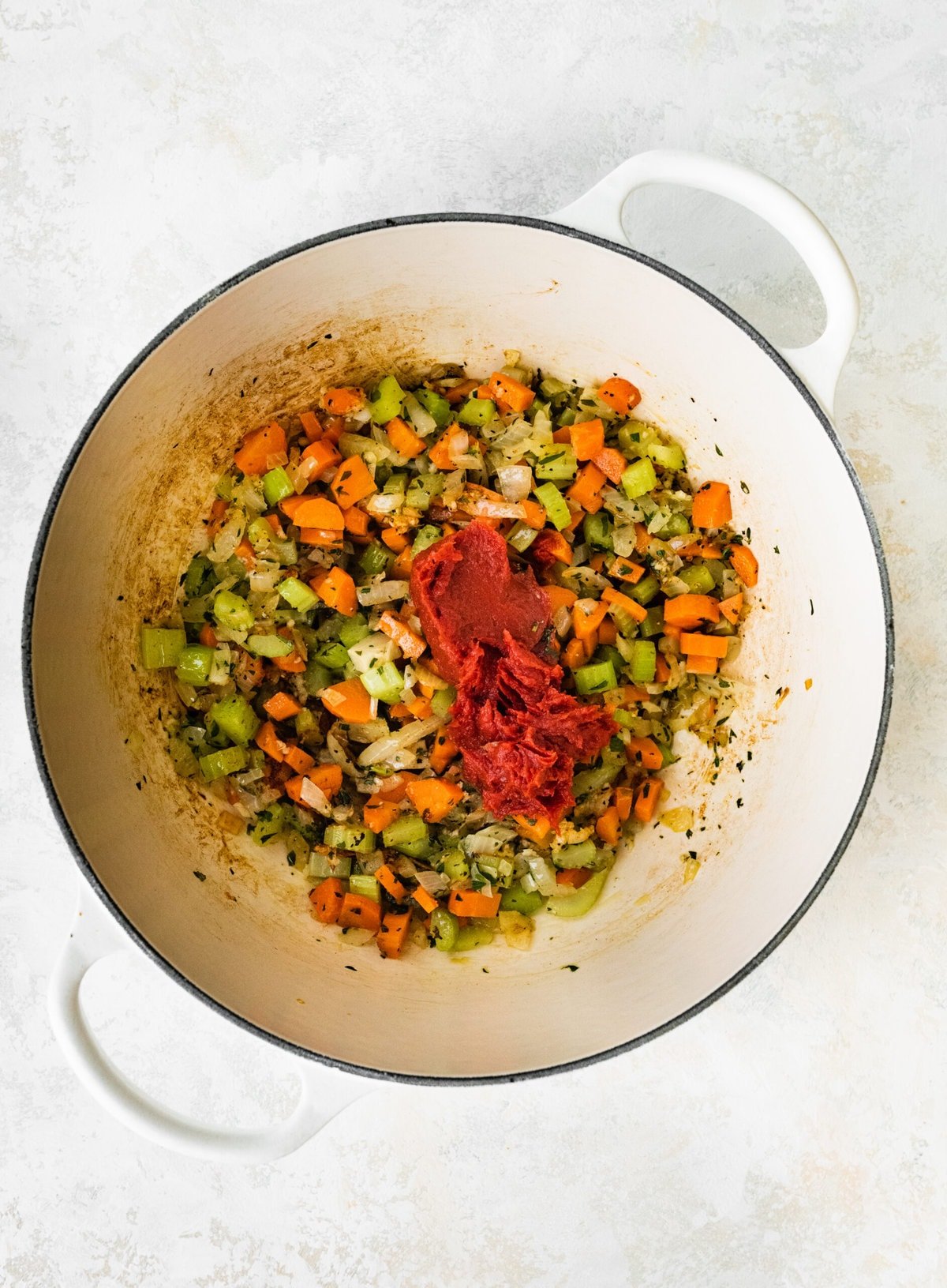 process of making classic lobster bisque: adding tomato paste to softened vegetables in pan.