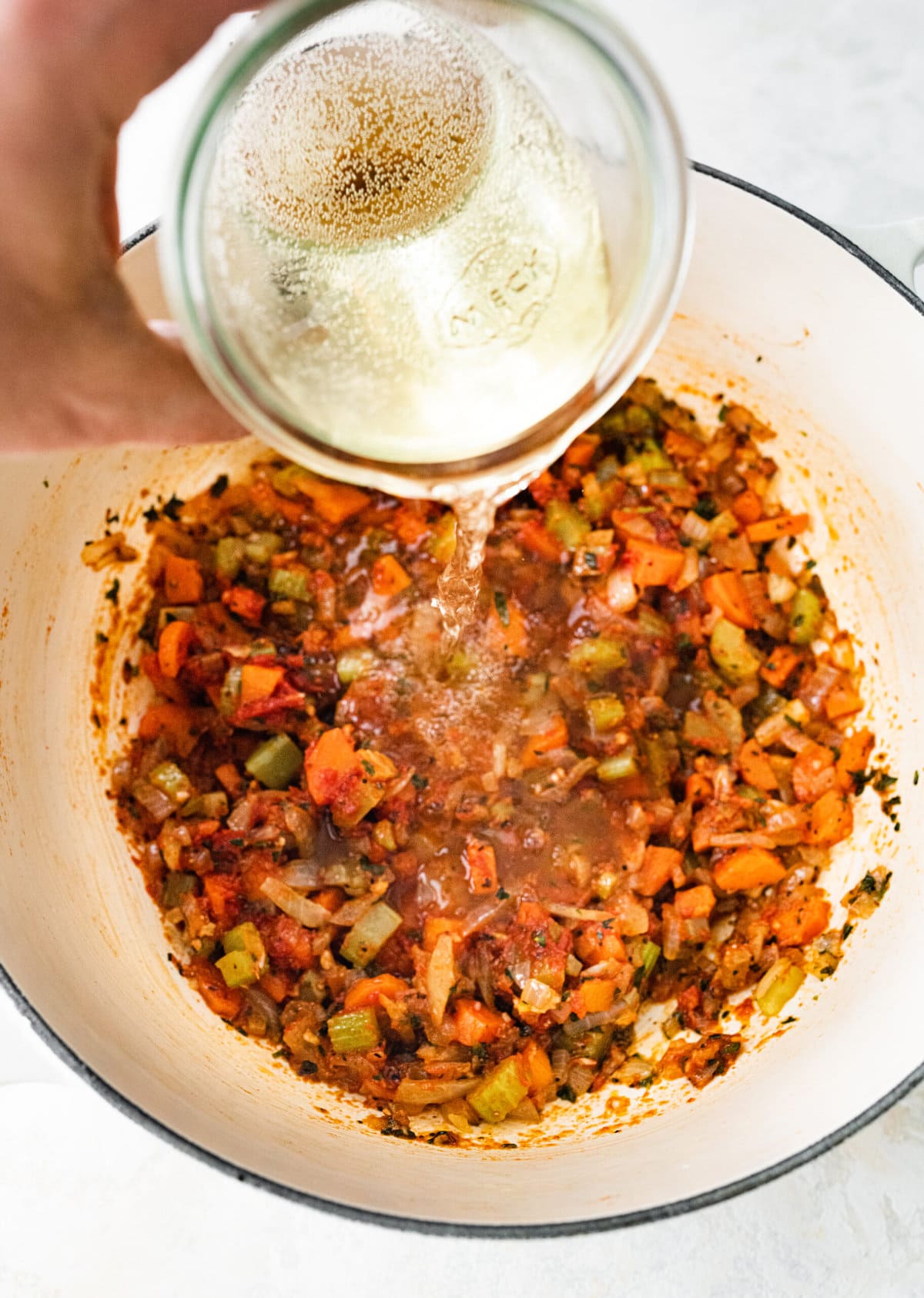 process of making classic lobster bisque: adding wine to cooked vegetables.