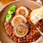 plateed braciole beef roll in a bowl with sauce and bread.