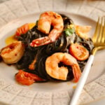 Fork on a plate with squid ink pasta with seafood and cherry tomato sauce.