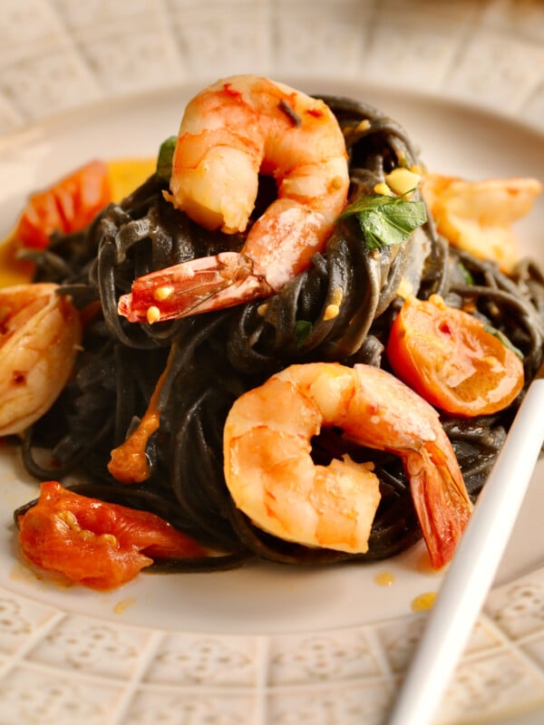 Fork on a plate with squid ink pasta with seafood and cherry tomato sauce.