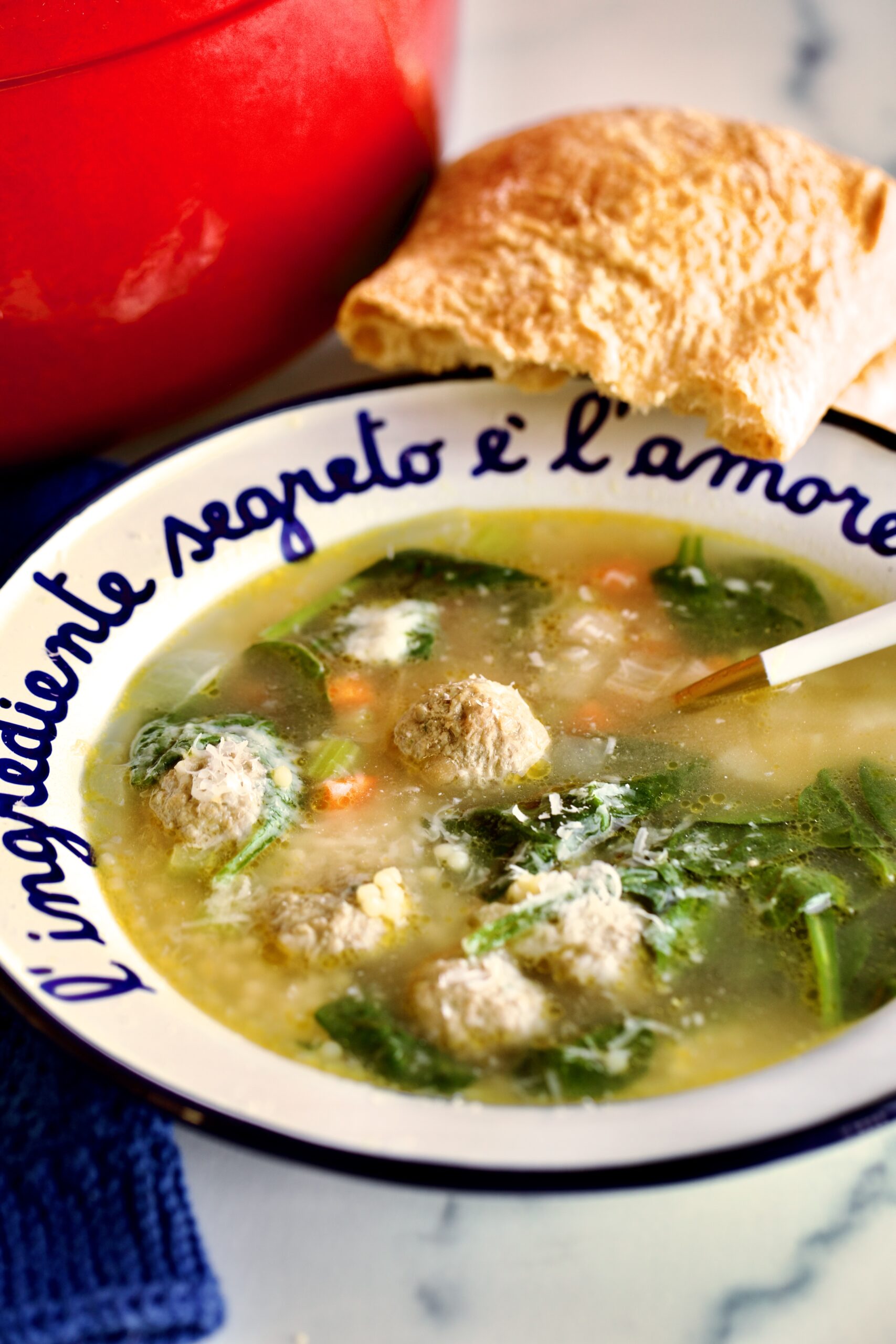 Classic Italian Wedding Soup Recipe in a bowl with spoon and bread in the background.