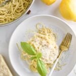 Lemon Butter Pasta Sauce (Pasta al Limone) in a serving bowl with basil on the side. Pan with pasta in the background and lemons as decoration.