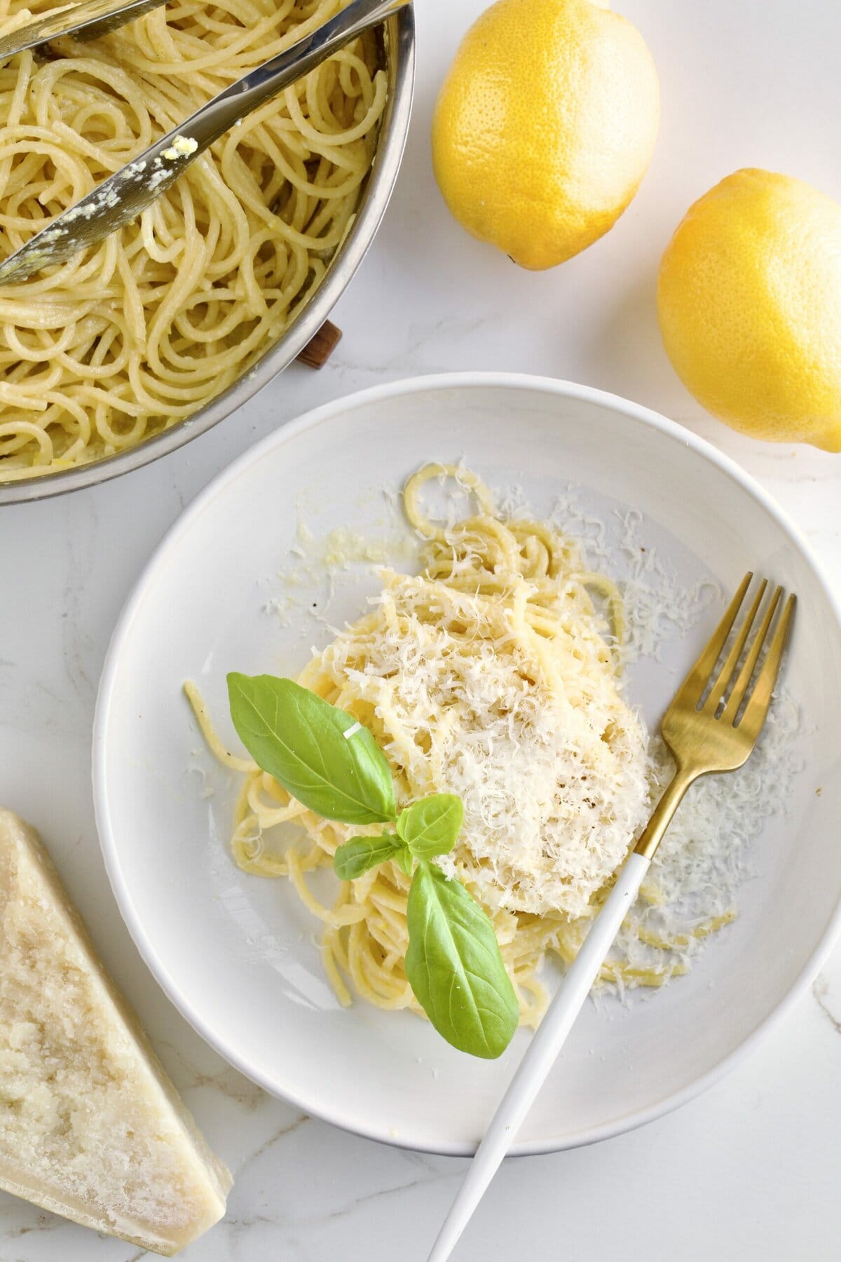 Lemon Butter Pasta Sauce (Pasta al Limone) in a serving bowl with basil on the side. Pan with pasta in the background and lemons as decoration.