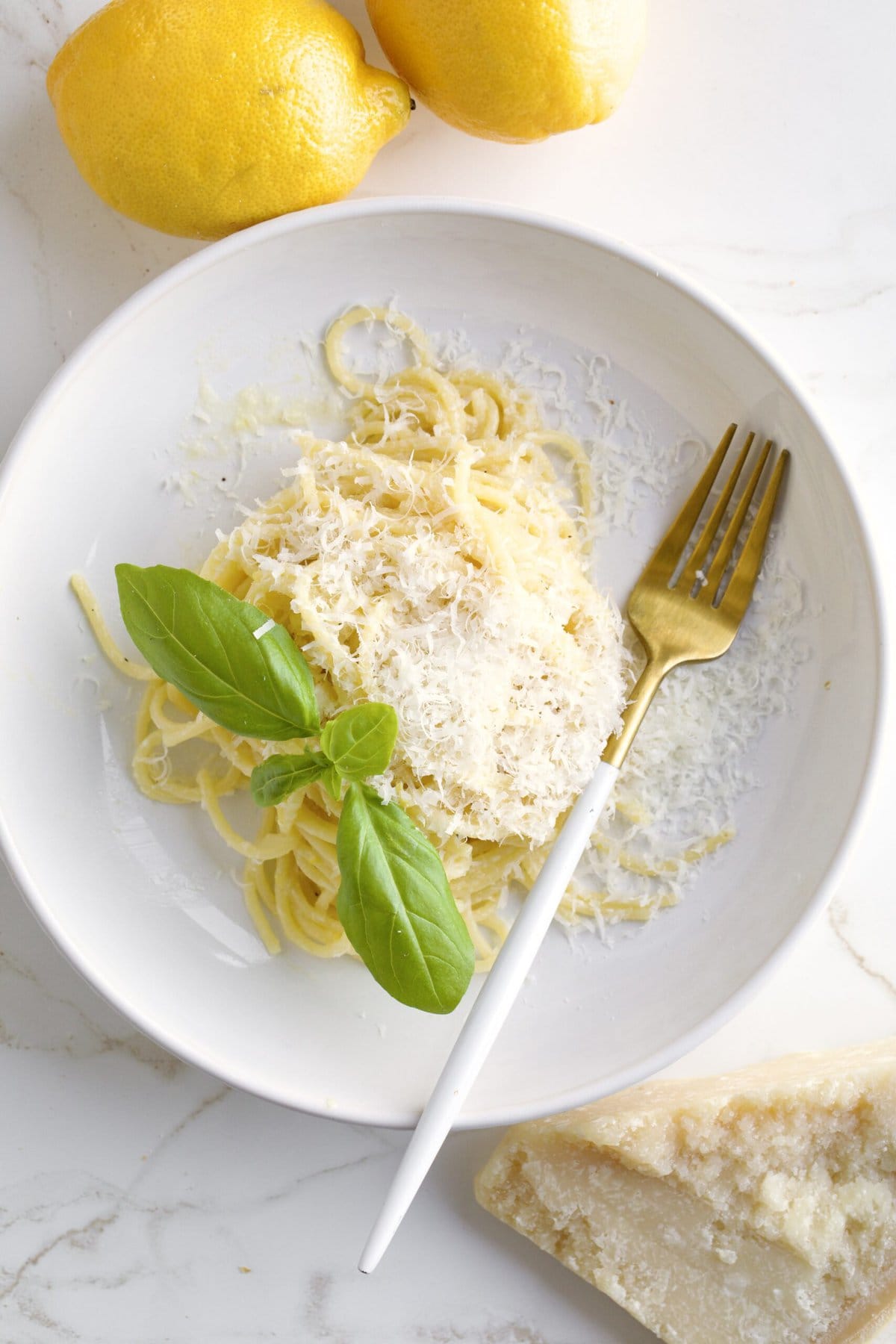 Lemon Butter Pasta Sauce (Pasta al Limone) in a serving bowl with basil on the side and fork in the plate. Real parmigiano on the side and lemons in the background.