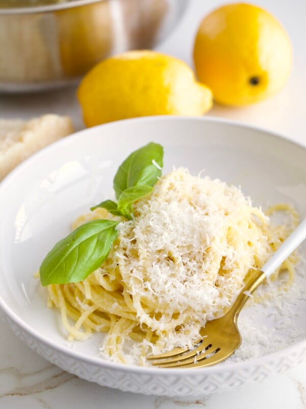 Lemon Butter Pasta Sauce (Pasta al Limone) in a serving bowl with basil on the side. Pan with pasta in the background and lemons as decoration.