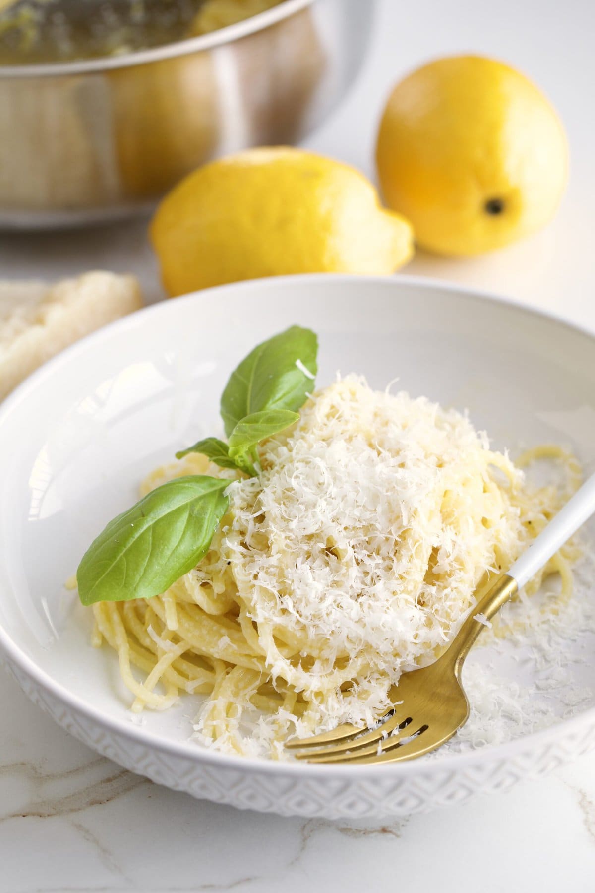 Lemon Butter Pasta Sauce (Pasta al Limone) in a serving bowl with basil on the side. Pan with pasta in the background and lemons as decoration.