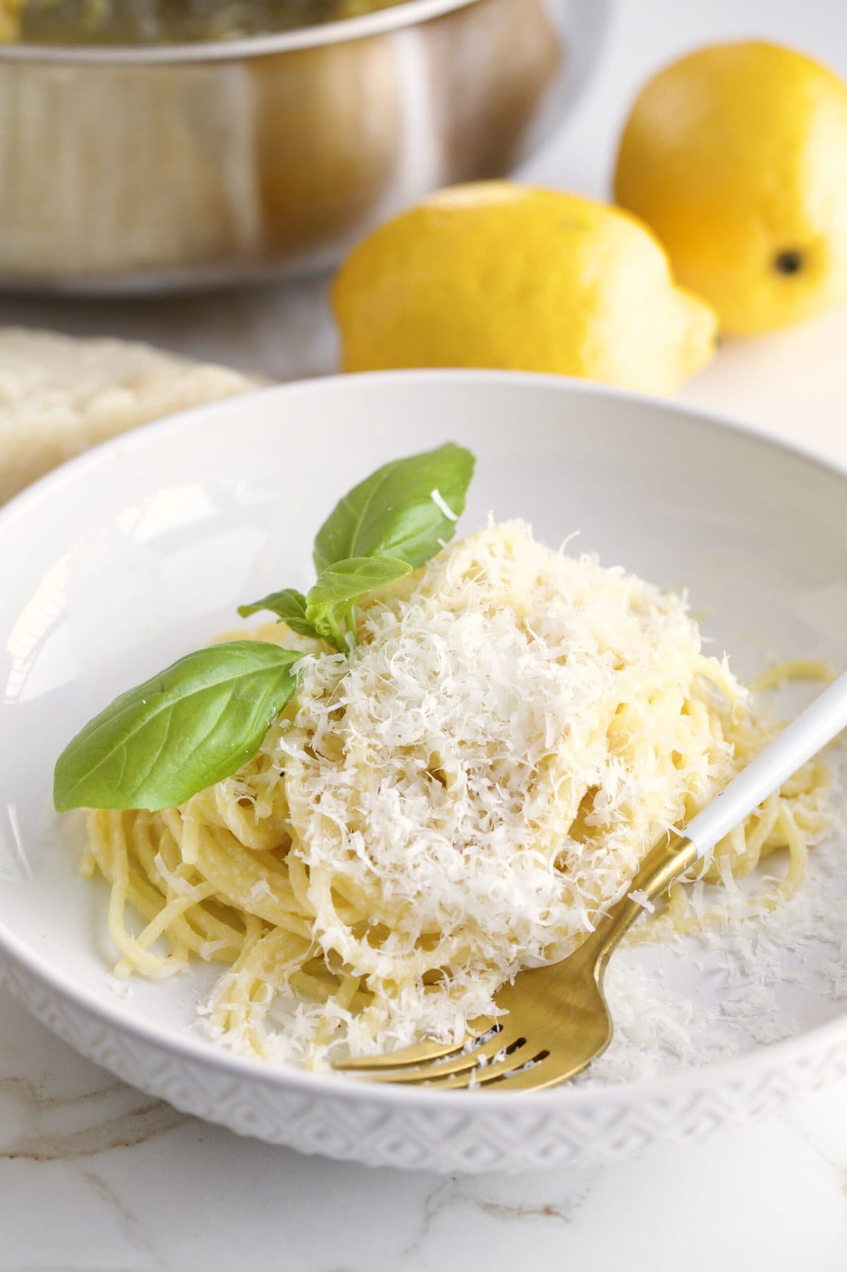 Lemon Butter Pasta Sauce (Pasta al Limone) in a serving bowl with basil on the side. Pan with pasta in the background and lemons as decoration.