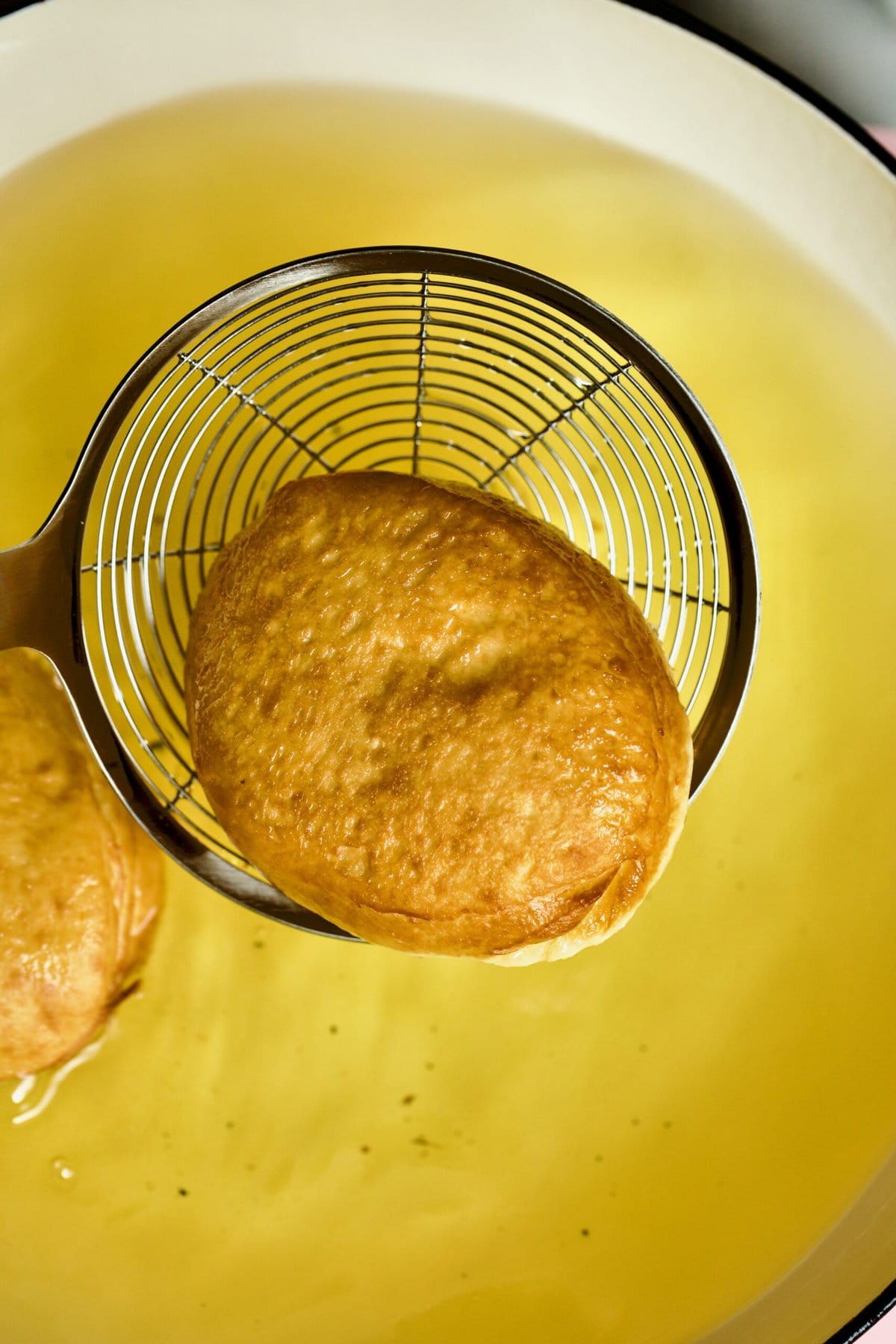 Process of making Bomboloni (how to make bomboloni recipe)- frying the donuts in oil- taking out with slotted spoon.