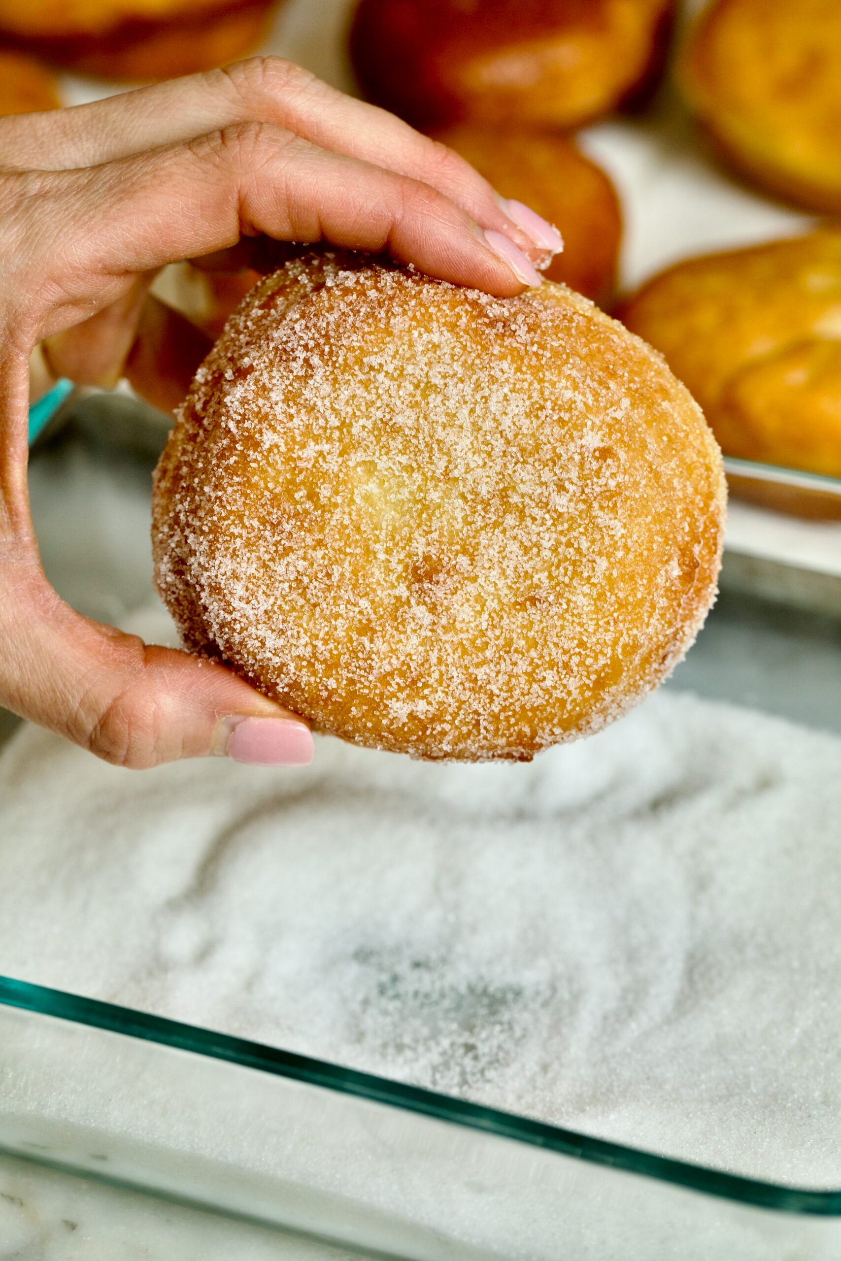 Process of making Bomboloni (how to make bomboloni recipe)- rolling the warm donut in sugar with hands.