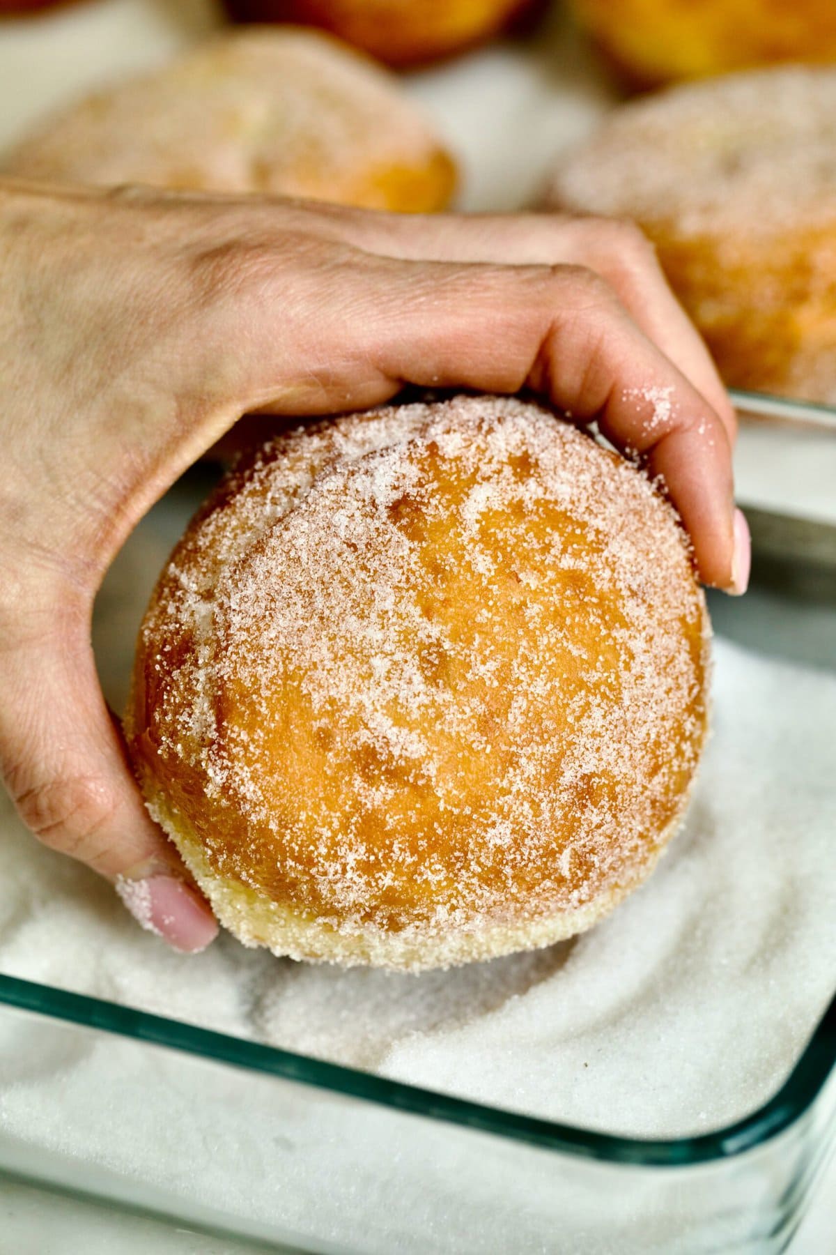 Process of making Bomboloni (how to make bomboloni recipe)- rolling the warm donut in sugar with hands.