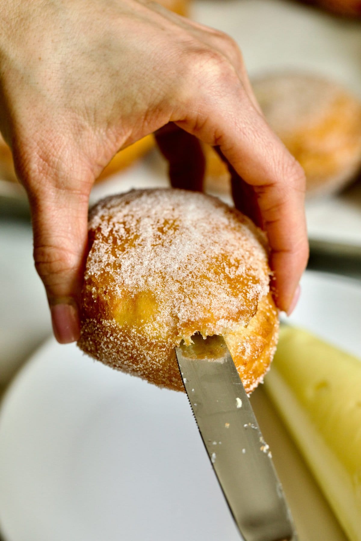 Process of making Bomboloni (how to make bomboloni recipe)- making a hole in the donut with a knife to put cream inside.