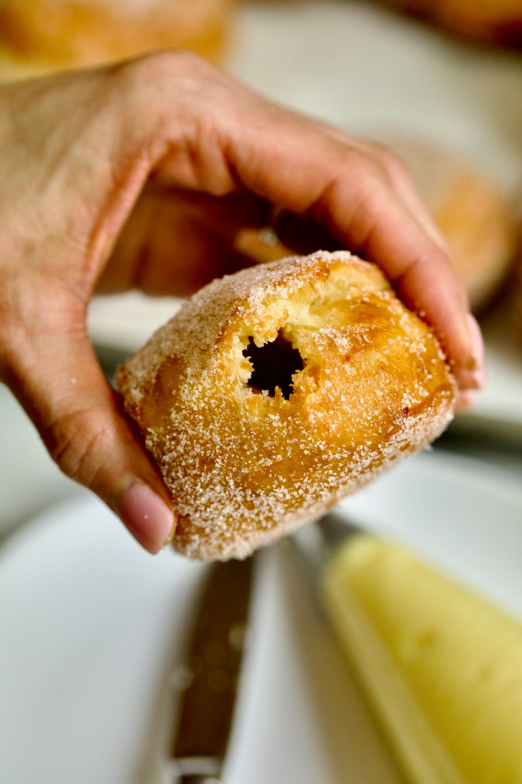 Process of making Bomboloni (how to make bomboloni recipe)- hands holding donut with hole in the middle ready to fill with cream.