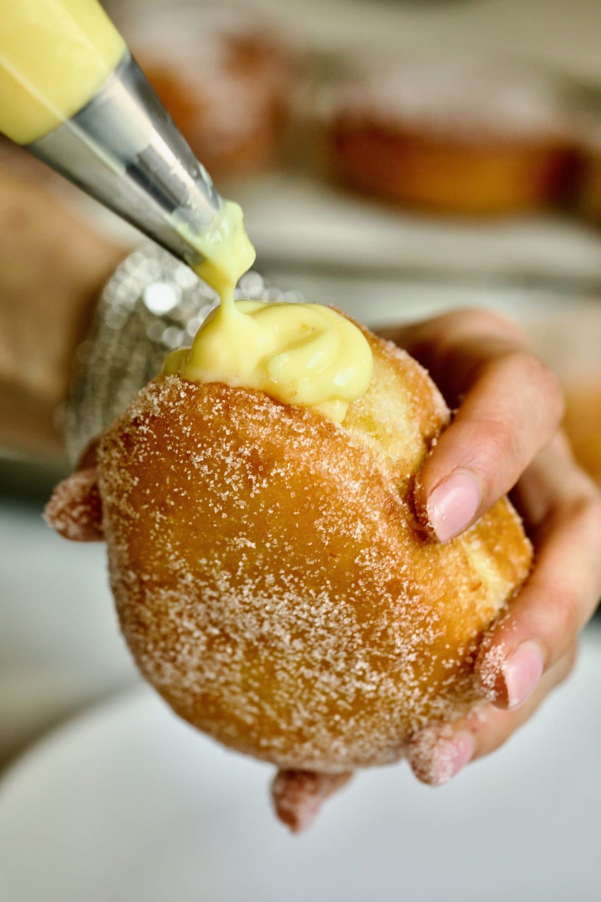 Process of making Bomboloni (how to make bomboloni recipe)- filling the donut with Italian pastry cream with a pastry bag. Hands holding the donut.