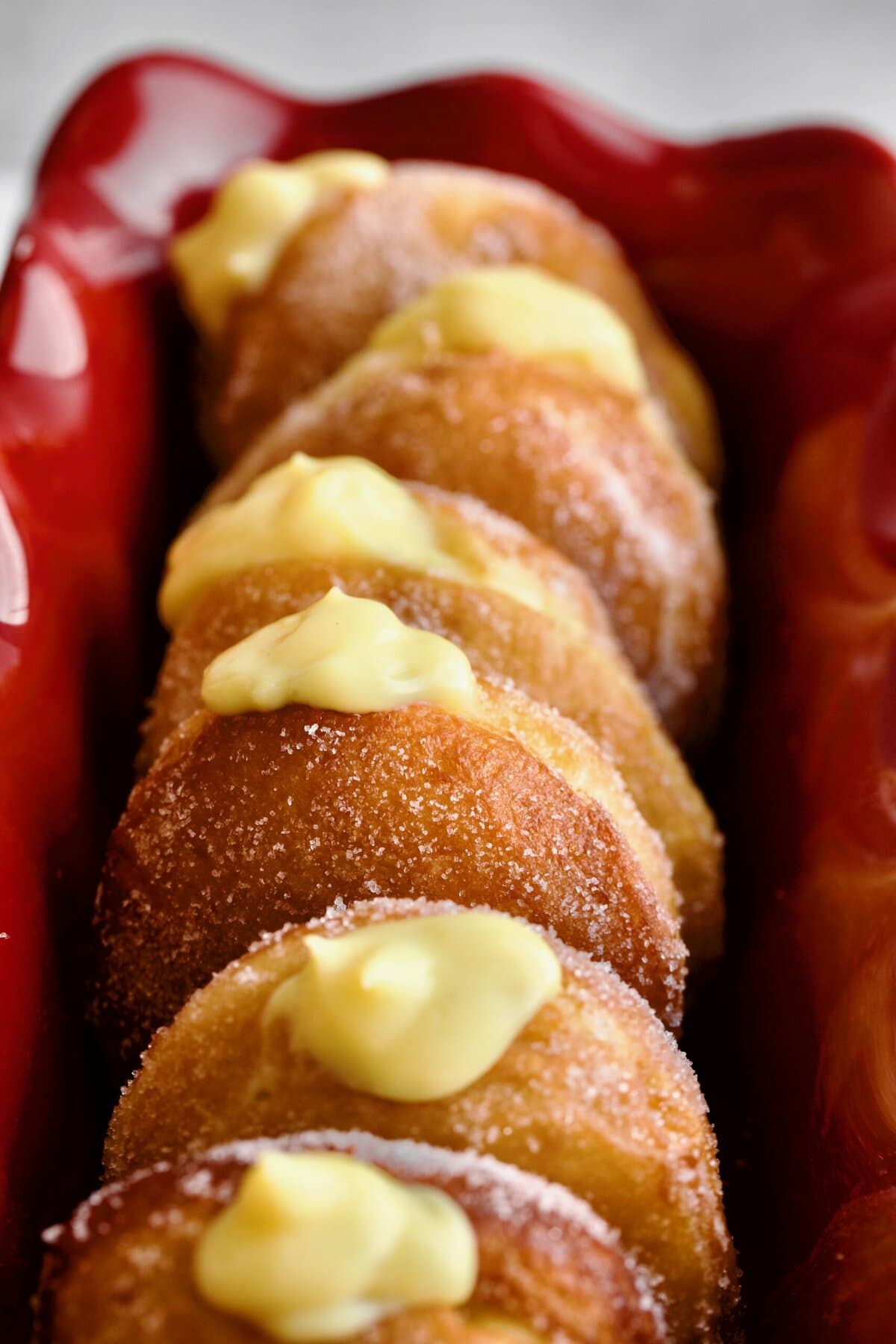 Bomboloni Recipe (Italian Donuts with Cream Filling) in a red ruffled narrow cake pan. Cream coming out of the top of the donuts.
