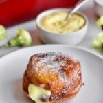 one bomboloni recipe on a plate with pastry cream in the backound and yellow flowers as decoration.