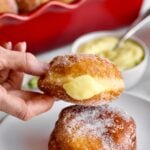 hands holding a bomboloni donut with cream in the middle.