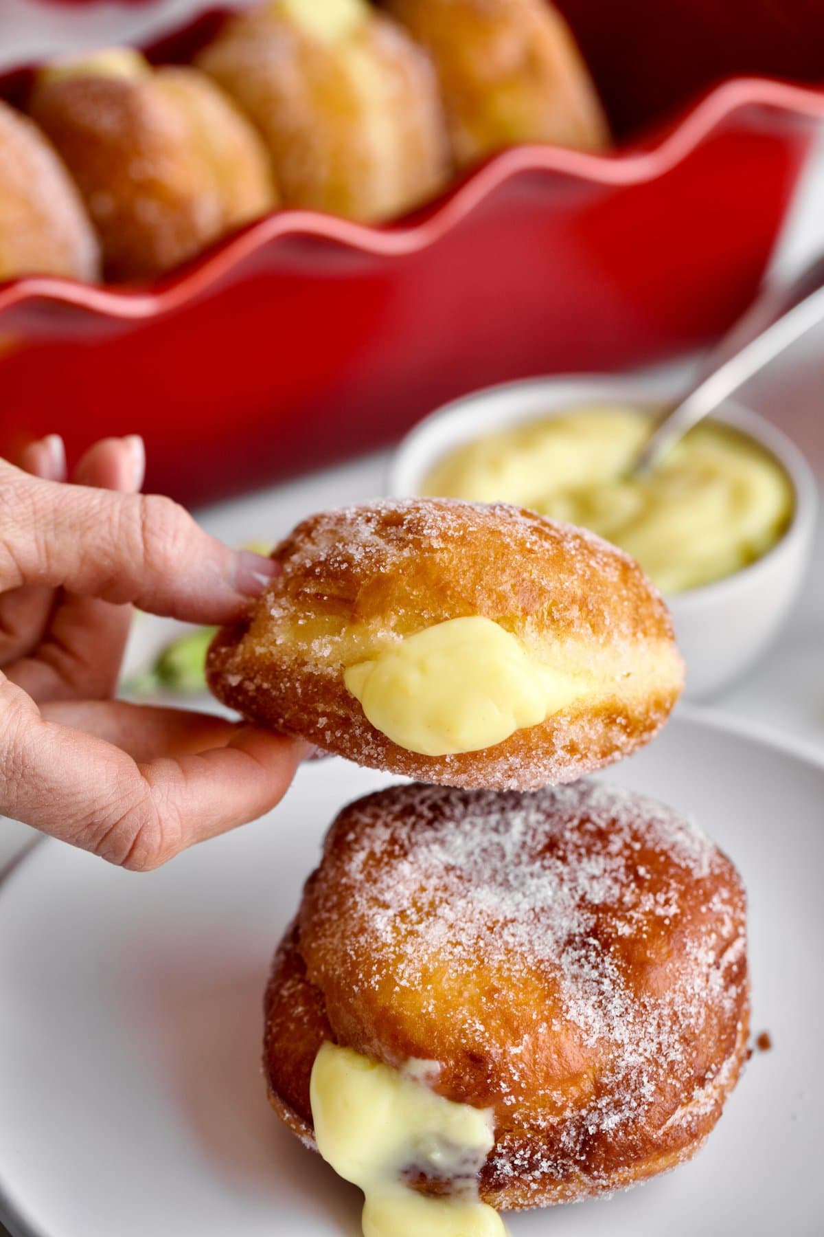hands holding a bomboloni donut with cream in the middle.