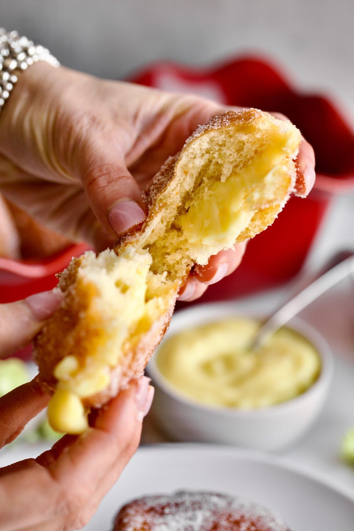 inside of the bomboloni donut with cream in the middle. Hands holding torn open donut with cream.