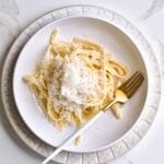 Fork on a plate with Italian fettucine alfredo topped with grated cheese.