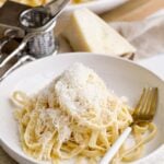 Fork in a bowl of Italian fettucine alfredo topped with cheese.