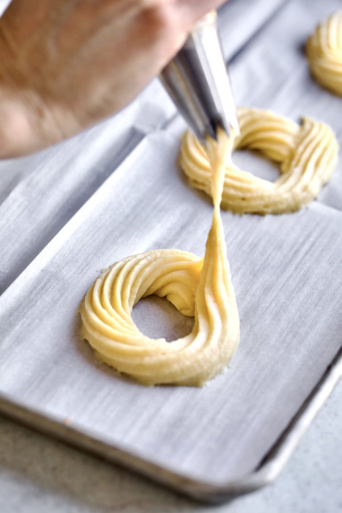 Process of making Baked Zeppole Di San Giuseppe Recipe (Italian)- piping choux pastry on parchment lined cookie sheet into a round donut like shape.