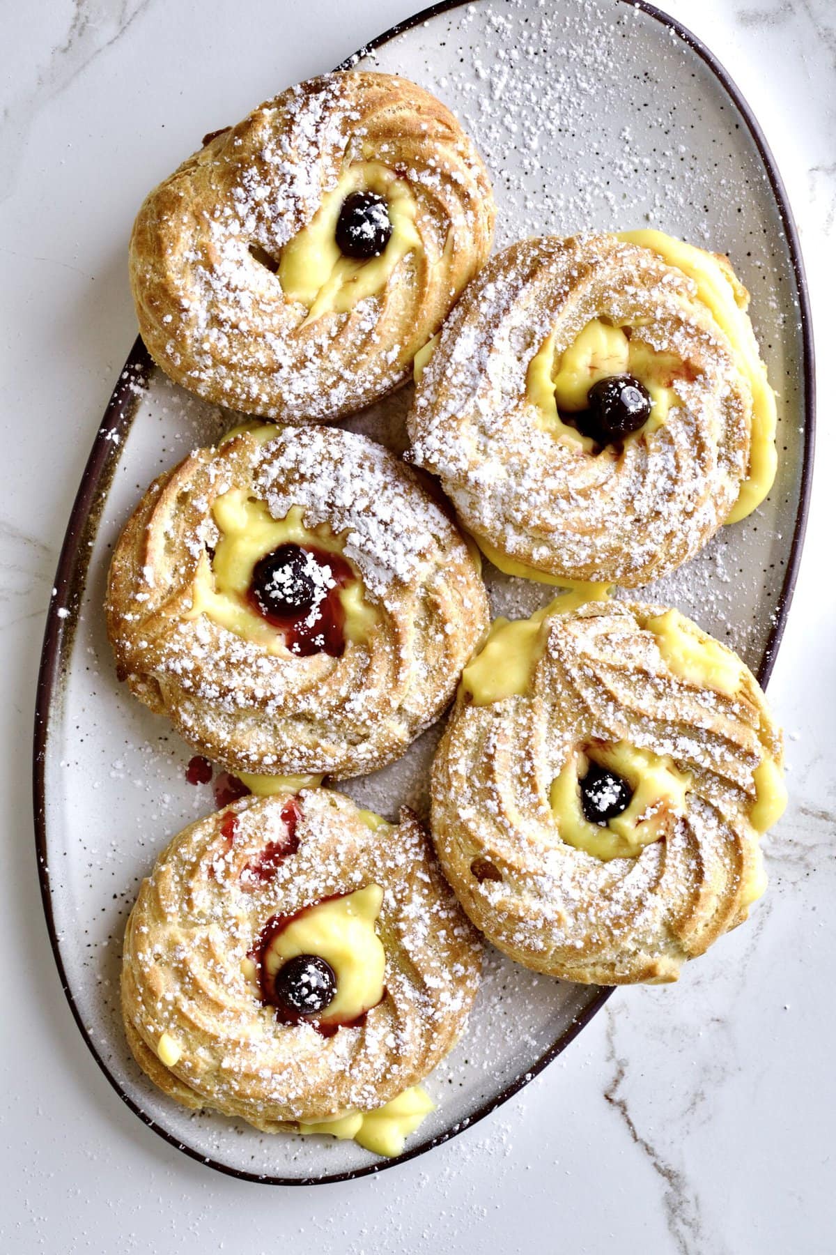 finish zeppole di san Giuseppe on a serving platter with cream and Amarena cherries on top.