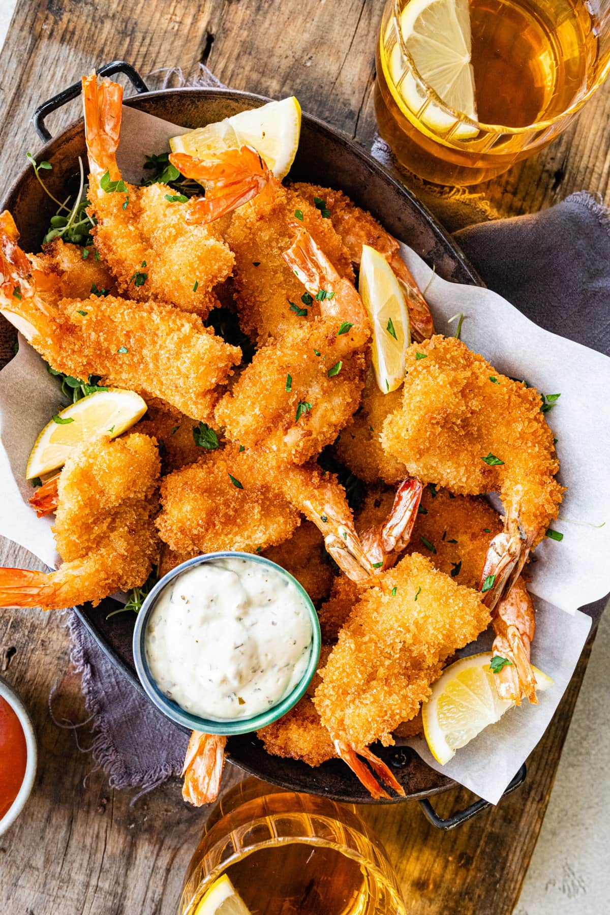 Fried shrimp on serving platter with lemon wedges, parsley, and tartar sauce. Glas of water with lemon in it.