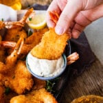 Hand dipping fried shrimp into tartar sauce.