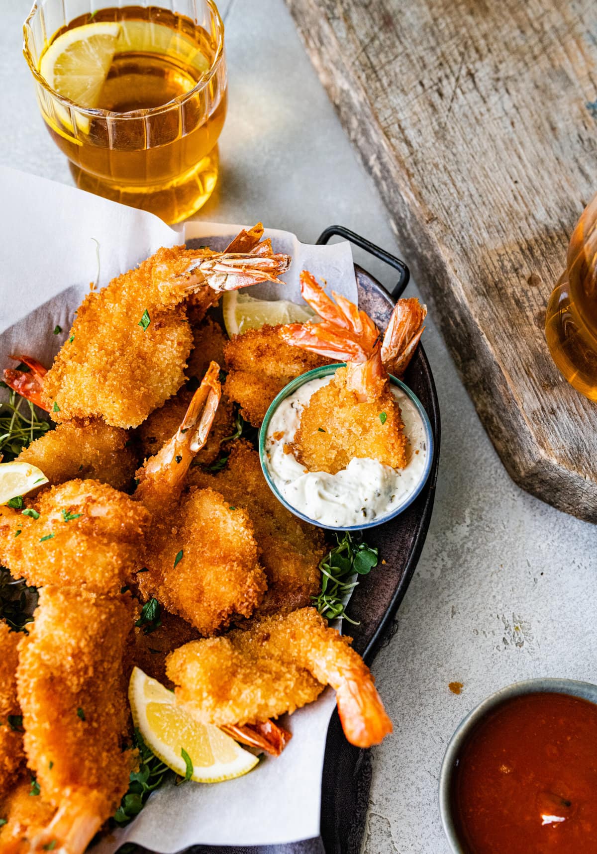 baket of fried shrimp with one shrimp in the tartar sauce. Two glasses of water with lemon surrounding it.