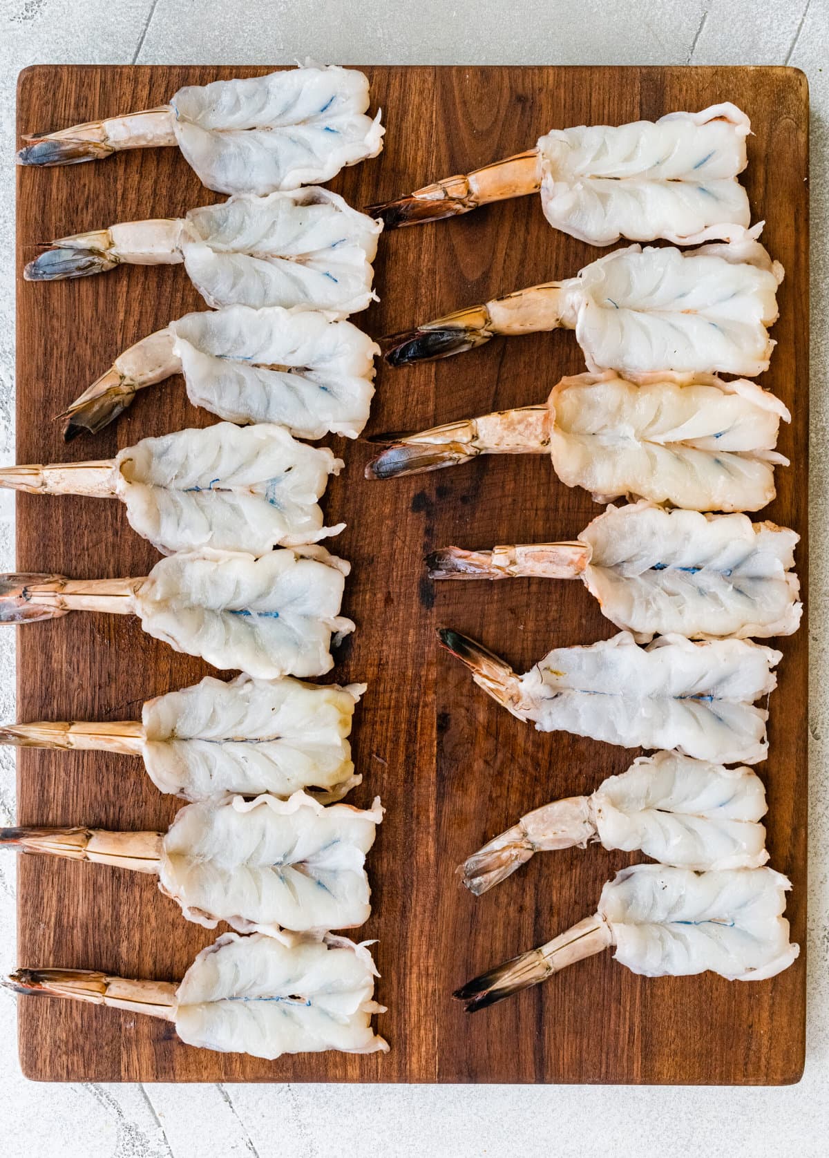 process for how to make Fried Butterfly Shrimp Recipe (Easy and Crunchy)- all shrimp butterflied on a wood cutting board.