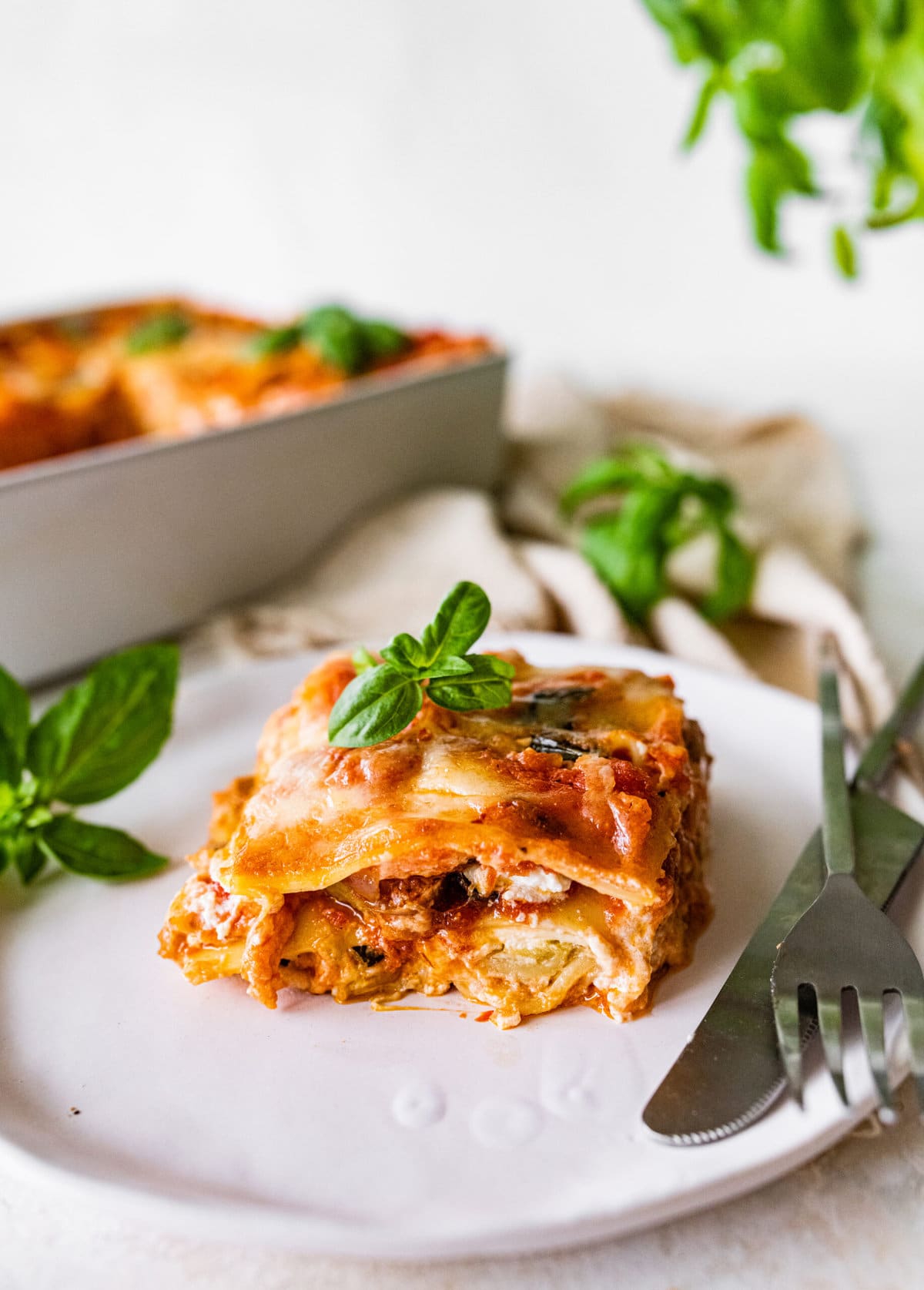 Easy Mediterranean Lasagna slice on a plate ready to eat. Fork and knife on the plate.
