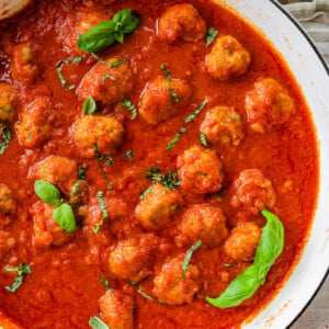 finished sausage meatballs done cooking in the sauce. Basil leaves on top for garnish.